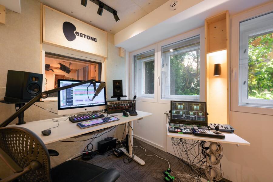 Studio 2: a desk with a computer, two monitor speakers and a microphone on a boom arm, a control desk beside it and windows onto the garden.