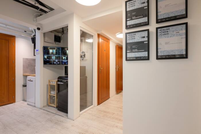 The corridor and kitchenette, with a screen showing the camera feeds and framed certificates on the wall.